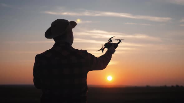 Silhouette of a Farmer Using a Drone in a Wheat Field at Sunset. Concept Technology Innovations for