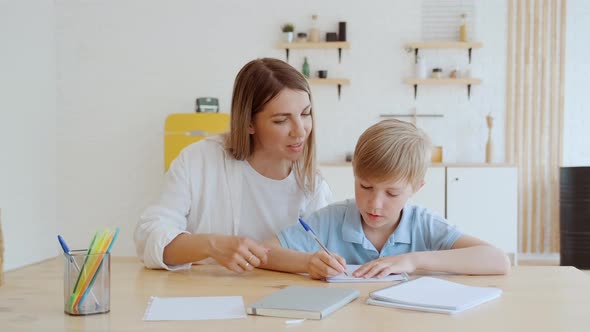 Young Mother Helping Her Son to Do His Homework at Home They Sit at Table