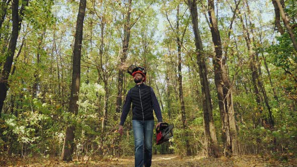 Man Holding a Chainsaw and Walking in a Forest