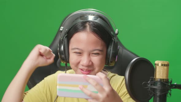 Kid Girl Playing Video Game With Mobile Phone Then Celebrating While Live Stream On Green Screen alt