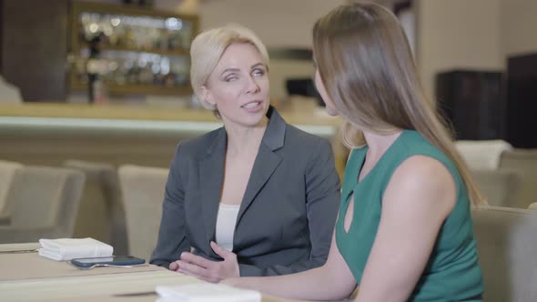 Portrait of Emotional Caucasian Blond Woman Talking and Gesturing As Sitting in Cafe with Brunette