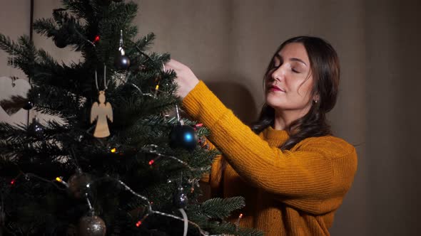 Young Woman in Mustard Sweater Decorates an Artificial Fir Tree