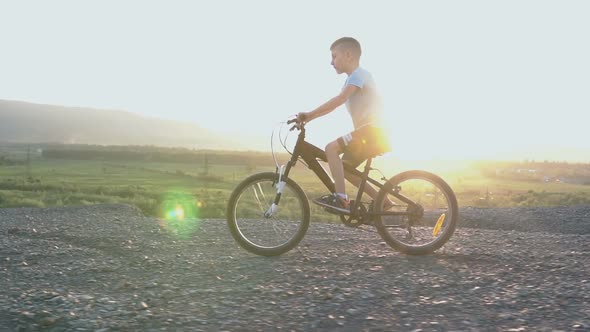 Little Kid Riding Bike in Summer Top of Mountain at Beautiful Sunset Sky Background alt