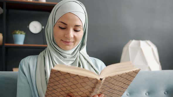 Portrait of Happy Young Muslim Lady Reading Book Enjoying Leisure Time in Cozy Room