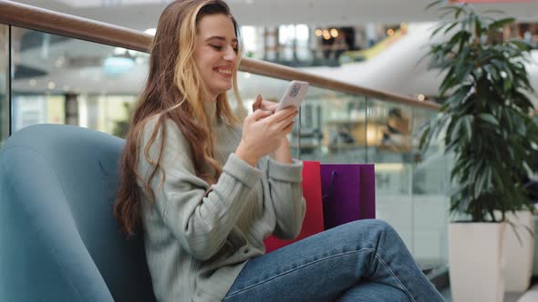 Cheerful Happy Young Girl Shopper Shopaholic Woman Sitting in Shopping Mall with Packages Looking at