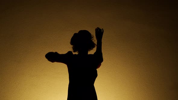 Shadow Of Girl Dancing Near The Wall. Woman Takes Off Her Coat.