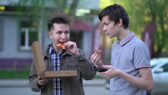 Two Friends are Eating Pizza Outdoors