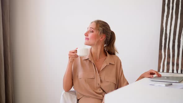 Woman Enjoys Cup of Hot Drink Sitting at Office Table