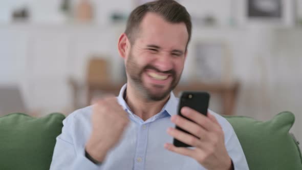 Young Man Celebrating on Smartphone at Home 