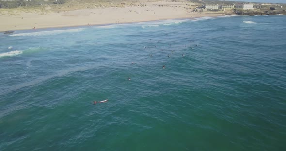 Aerial drone shot flying over surfers on the waves of the atlantic ocean, at sunset, in praia do Gui