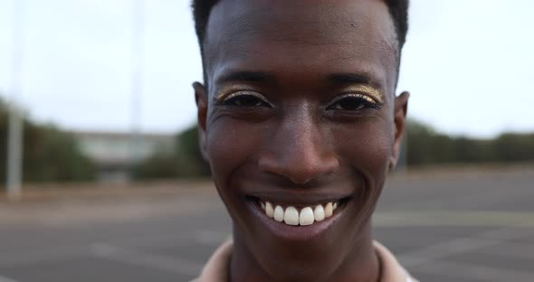 Happy gay african man with make-up smiling on camera outdoor
