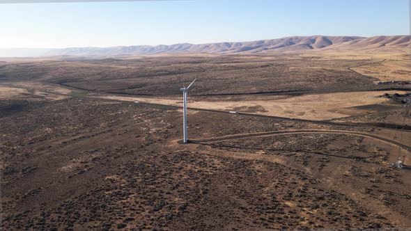 Slow aerial pull of a lone electric wind turbine next to a long desert highway