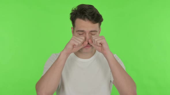 Tired Young Man Rubbing Eyes on Green Background