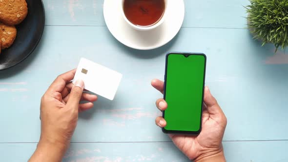 Holding Smart Phone with Empty Screen and Credit Card on Table