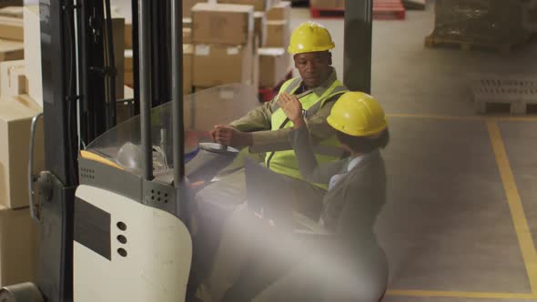 African american male and female workers wearing safety suits and using laptop in warehouse