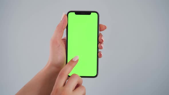 Female Hands Using a Smartphone with a Green Screen on a Gray Background. Chroma Key