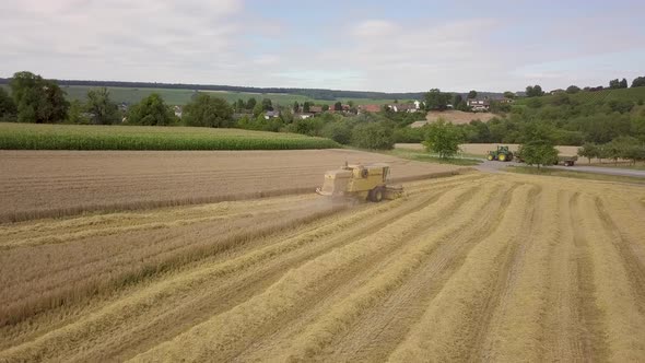 Harvester filmed from the side during crop. In the background a tractor ising by with two trailers f