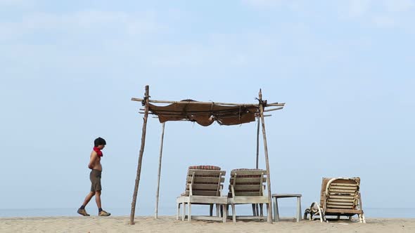 View of man walking by sea hut on beach in Goa.