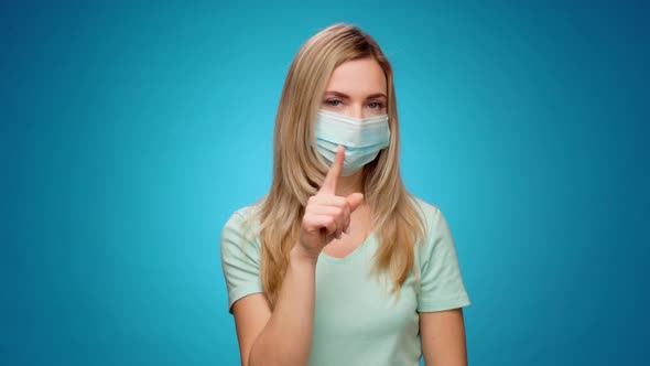 Pretty Woman in Medical Mask Does Disapproving Gesture with Her Finger Against Blue Background