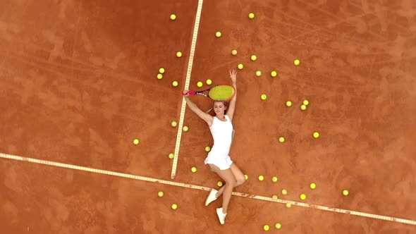 Girl relaxing on tennis court with a lot of balls and racket after hard tennis trainingg outdoor