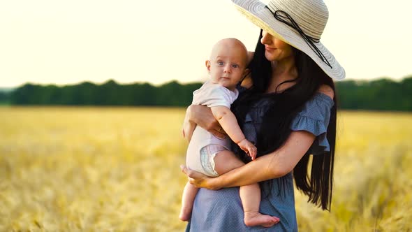Loving mother holding and kissing sweet baby in wheat field