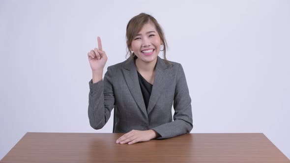 Young Happy Asian Businesswoman Pointing Up at Desk