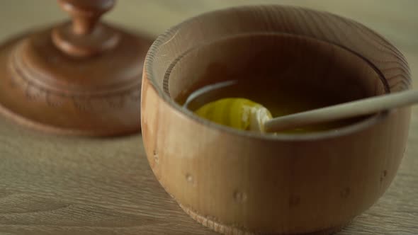 Honey Dripping Pouring From Honey Dipper in Wooden Bowl