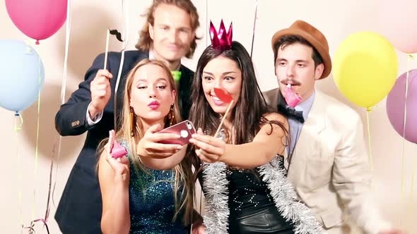 Group of happy friends taking selfie in photo booth