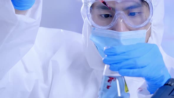 Scientist in PPE suite doing some research checking a liquid in a test tube at laboratory.