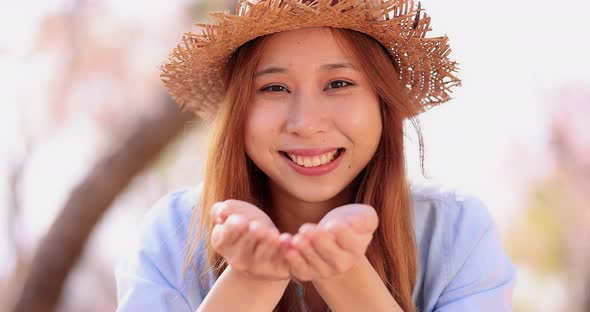 Slow motion happy smiling girl blowing on Sakura flower petals, making them fly to camera.