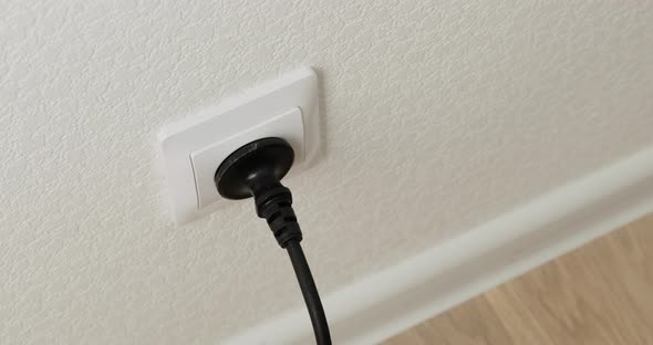 Hand Inserting black Power Plug into an white Electricity Socket. Close up.