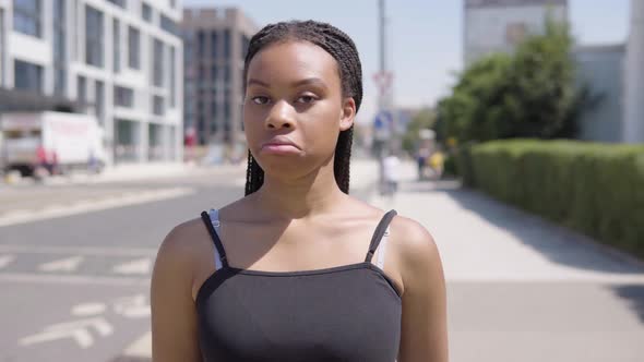 A Young Black Woman Frowns and Shakes Her Head at the Camera - a Townscape in the Blurry Background