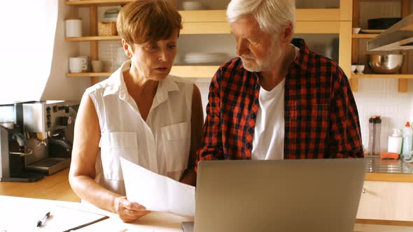 Senior couple paying bills online on laptop in kitchen