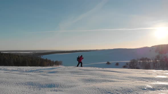 A Man with Backpack and Trekking Sticks Against the Backdrop of Winter Mountains, Beautiful Sunset