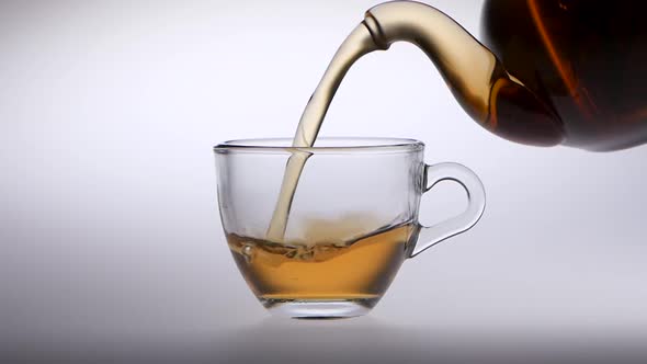 Tea Is Poured From a Teapot Into Transparent Glass Cup