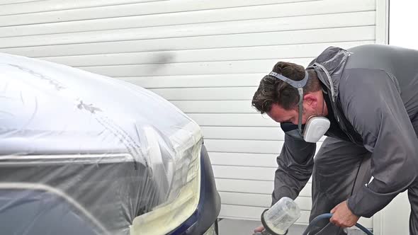 Man spray painting front and side of vehicle with varnish. Slow motion handheld view