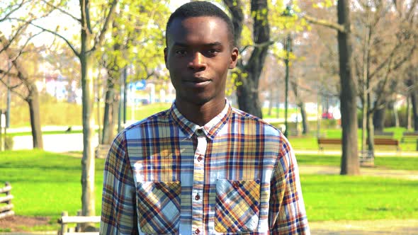 A Young Black Man Smiles and Shows a Thumb Up To the Camera in a Park on a Sunny Day