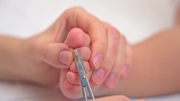 Mother's hands with scissors cut the toenails of a sleeping baby, selective focus
