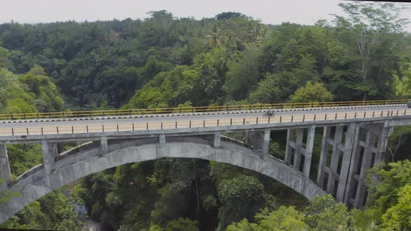 Drone View of Motorbikes Crossing Suspension Bridge Leading To Tropical Forest