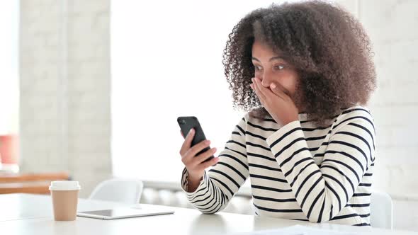 Excited African Woman Celebrating Success on Smartphone 