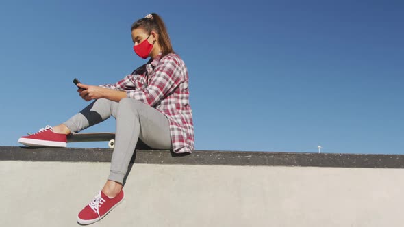 Caucasian woman wearing face mask, sitting and using smartphone