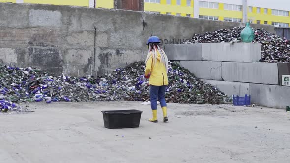 Woman in Hard Hat with Dreadlocks Standing Against the Pile of Broken Glass Used Bottles Next to the