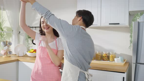 Asian attractive couple man and woman listen to music, enjoy dance together in kitchen at home.