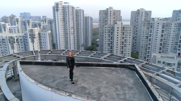 Aerial Orbital Shot of Beautiful Blond European Girl Standing on the Roof Top of Modern Apartments