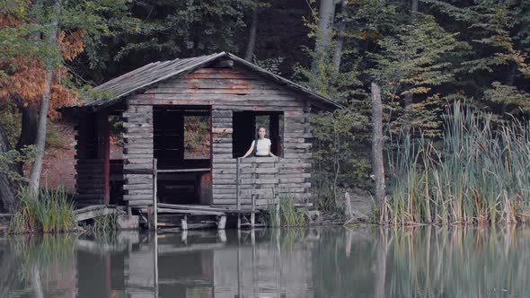 Young Woman Tourist Standing in the Wooden Little House Near the Lake