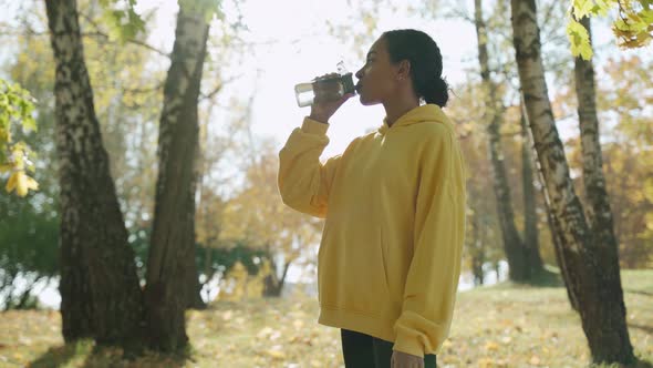 Young Girl Drinking Water Before Run at the Park in Sunny Autumn Morning