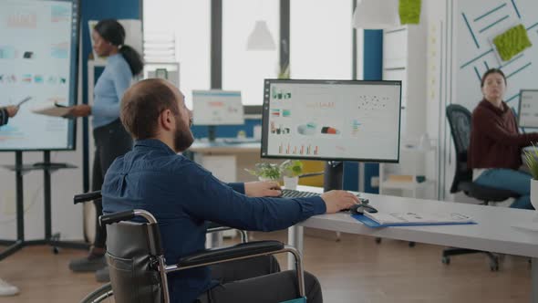 Businessman with Disabilities Asking Information to Woman Worker Typing on Pc