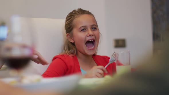 Happy caucasian sister laughing watching brother eating at table during family meal