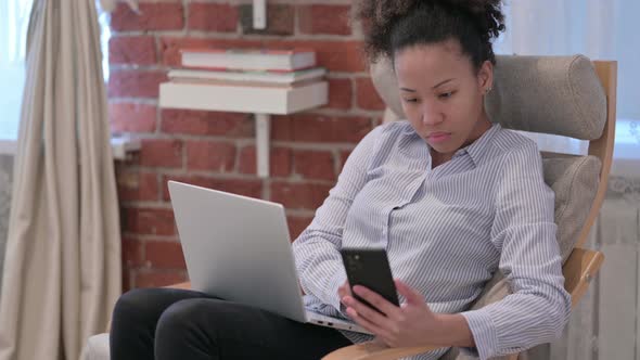 African American Woman with Laptop Using Smartphone