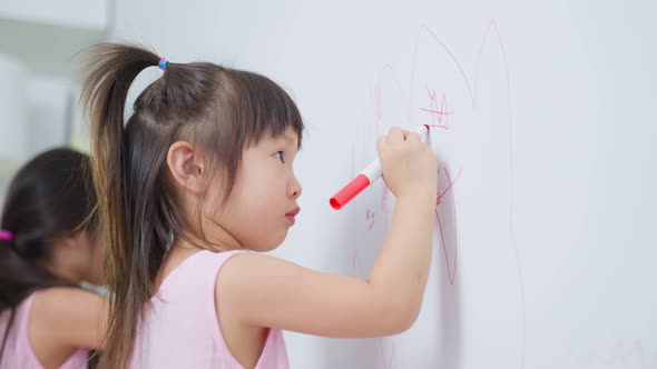 Asian young sibling kid girl enjoy paint on white wall in living room. alt